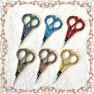 May include: Six decorative scissors with ornate metal handles in various colors, including gold, silver, blue, and red. The scissors have a heart-shaped design and are perfect for crafting or scrapbooking.