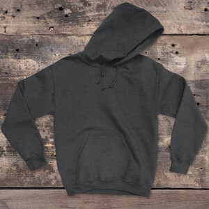 Puede incluir: Una sudadera con capucha de color gris oscuro con un bolsillo en la parte delantera. La sudadera est&aacute; colocada sobre una superficie de madera.
