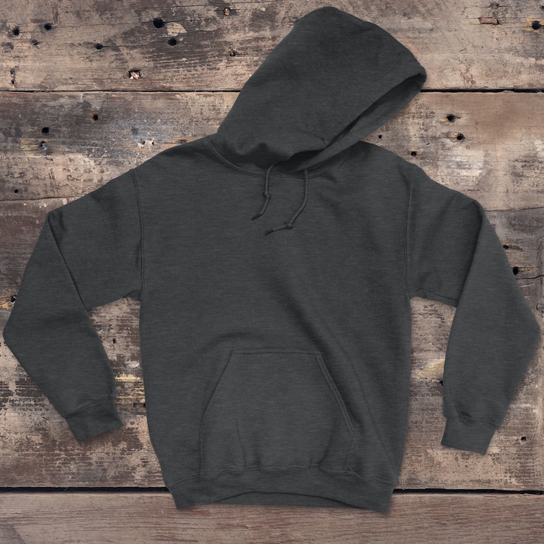 Puede incluir: Una sudadera con capucha de color gris oscuro con un bolsillo en la parte delantera. La sudadera est&aacute; colocada sobre una superficie de madera.