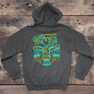 Puede incluir: Una sudadera con capucha gris oscuro con un dise&ntilde;o de p&aacute;jaro estilizado en color turquesa y amarillo en la espalda. El dise&ntilde;o recuerda al arte nativo americano.