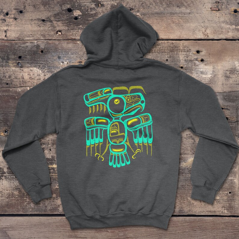 Puede incluir: Una sudadera con capucha gris oscuro con un dise&ntilde;o de p&aacute;jaro estilizado en color turquesa y amarillo en la espalda. El dise&ntilde;o recuerda al arte nativo americano.
