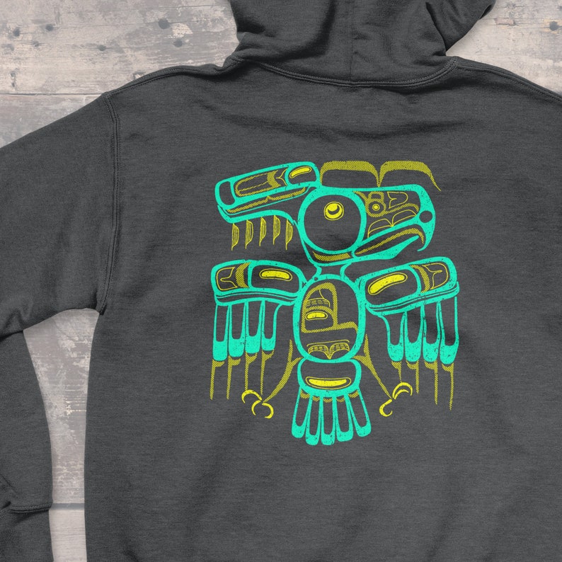 Puede incluir: Una sudadera con capucha gris oscuro con un dise&ntilde;o de p&aacute;jaro estilizado en turquesa y amarillo en la espalda.