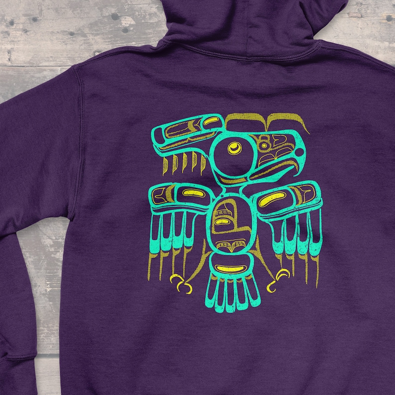 Puede incluir: Sudadera con capucha morada con un dise&ntilde;o de p&aacute;jaro estilizado en turquesa y dorado en la espalda.