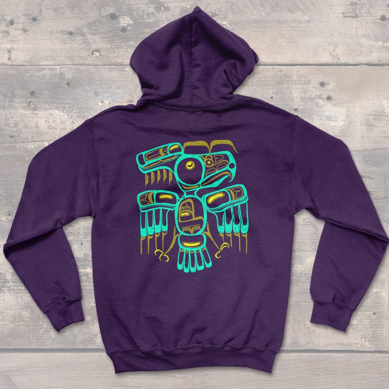 Puede incluir: Sudadera con capucha morada con un dise&ntilde;o nativo americano turquesa y dorado en la espalda. El dise&ntilde;o presenta un p&aacute;jaro estilizado con las alas extendidas.
