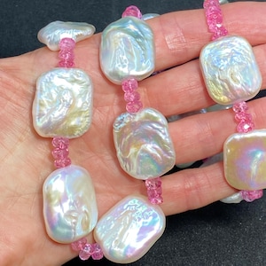 May include: A necklace featuring large, irregular, iridescent white pearls strung with small pink beads. The pearls have a unique, organic shape and reflect a range of colors. The pink beads add a pop of color to the design.