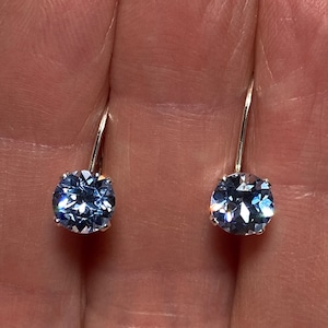 May include: A pair of silver dangle earrings with light blue round cubic zirconia stones.