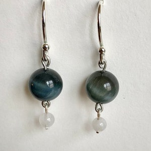 May include: A pair of silver hoop earrings with a dark blue gemstone and a smaller white gemstone dangling below.