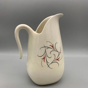 May include: A white ceramic pitcher with a curved handle and a stylized floral design in black and red.