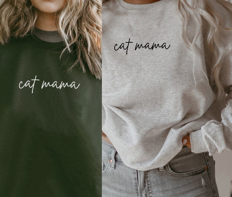 Pu&ograve; includere: Due donne indossano felpe con il testo "cat mama" in corsivo bianco. Una felpa &egrave; verde scuro e l'altra &egrave; grigio chiaro.