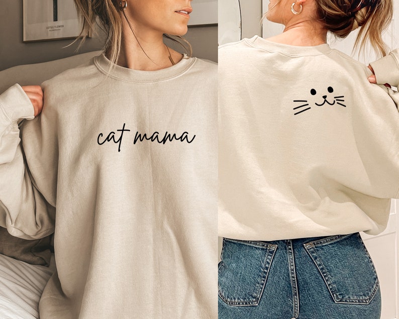 Pu&ograve; includere: Una felpa beige chiaro con la scritta "cat mama" stampata sul davanti e un viso di gatto nero sul retro.