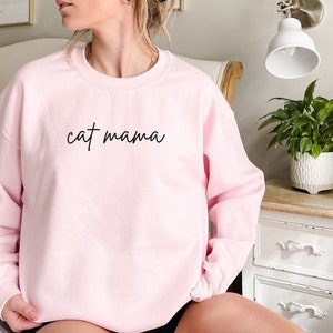 Pu&ograve; includere: Una felpa rosa con la scritta "cat mama" in corsivo nero.