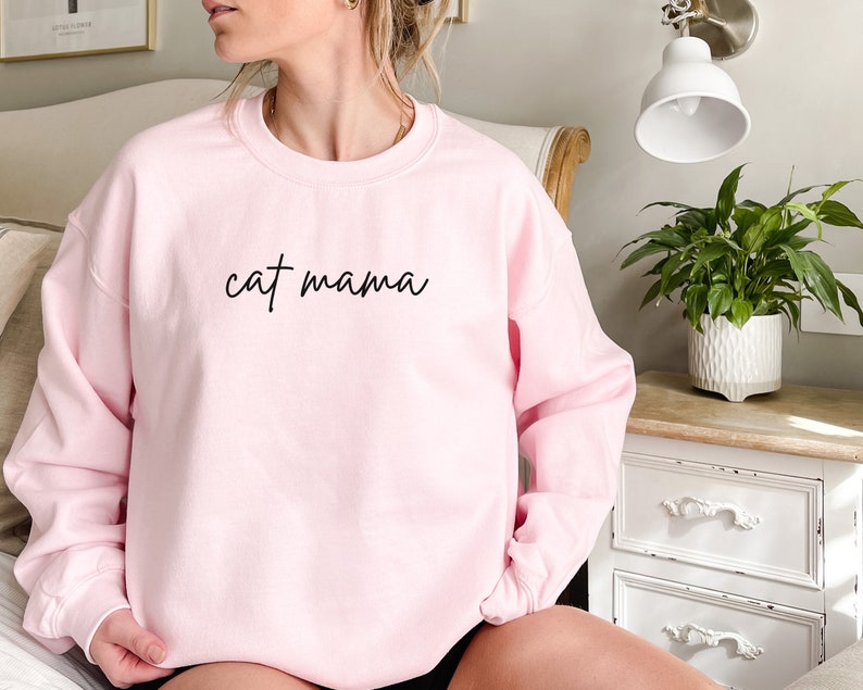 Pu&ograve; includere: Una felpa rosa con la scritta "cat mama" in corsivo nero.