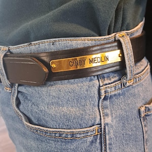 May include: A brown leather belt with a gold metal buckle engraved with the name "Cindy Medlin".