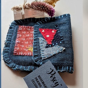 May include: Two small denim pouches with patchwork fabric designs. Each pouch has a tag attached with the text "Pisey" and a list of herbs: Rosemary, Prairie Gentian, and Celosia.