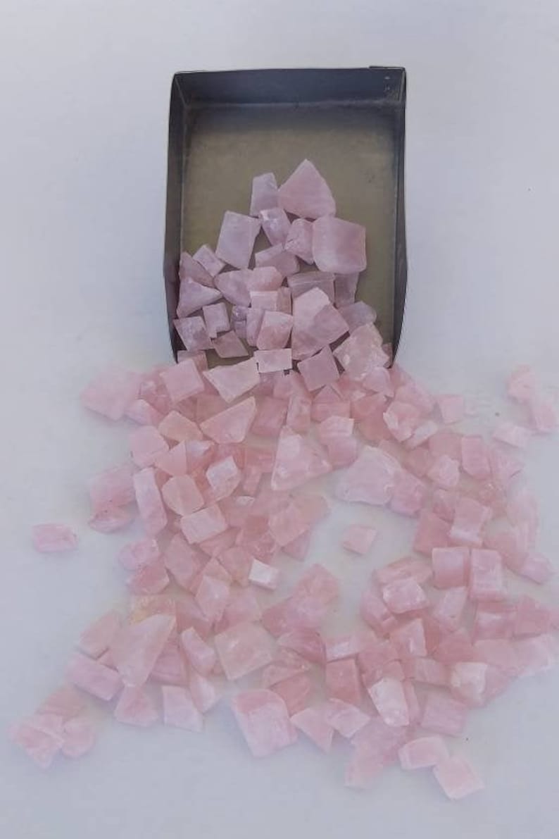 May include: A large pile of pink rose quartz crystals in various shapes and sizes. The crystals are loose and scattered on a white surface.