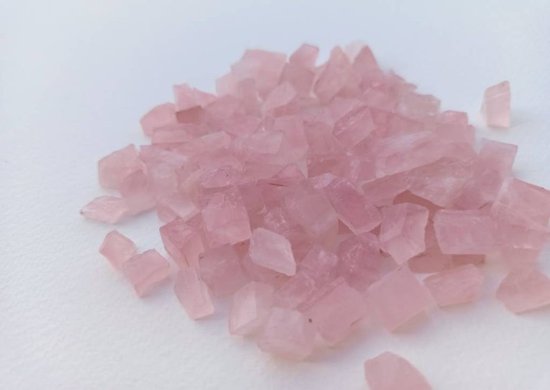 May include: A pile of small, light pink, irregularly shaped crystal chips.