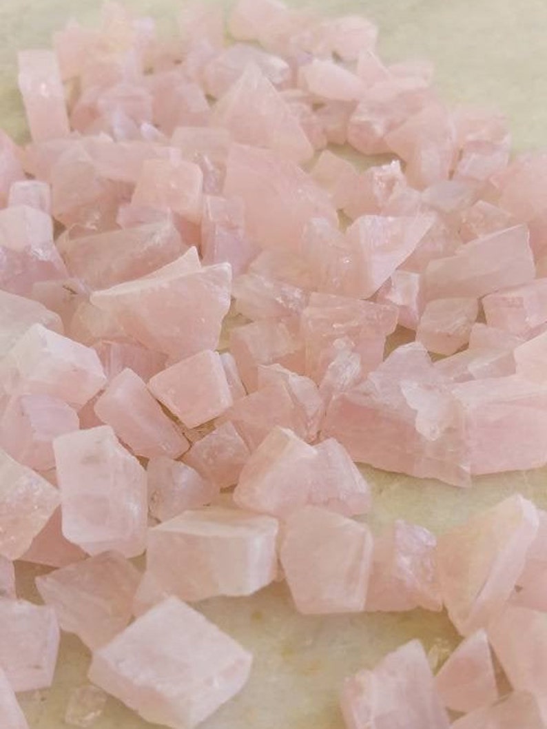 May include: A pile of pink rose quartz crystals, some are smooth and others are rough, all are tumbled and ready to be used for crafting or meditation.