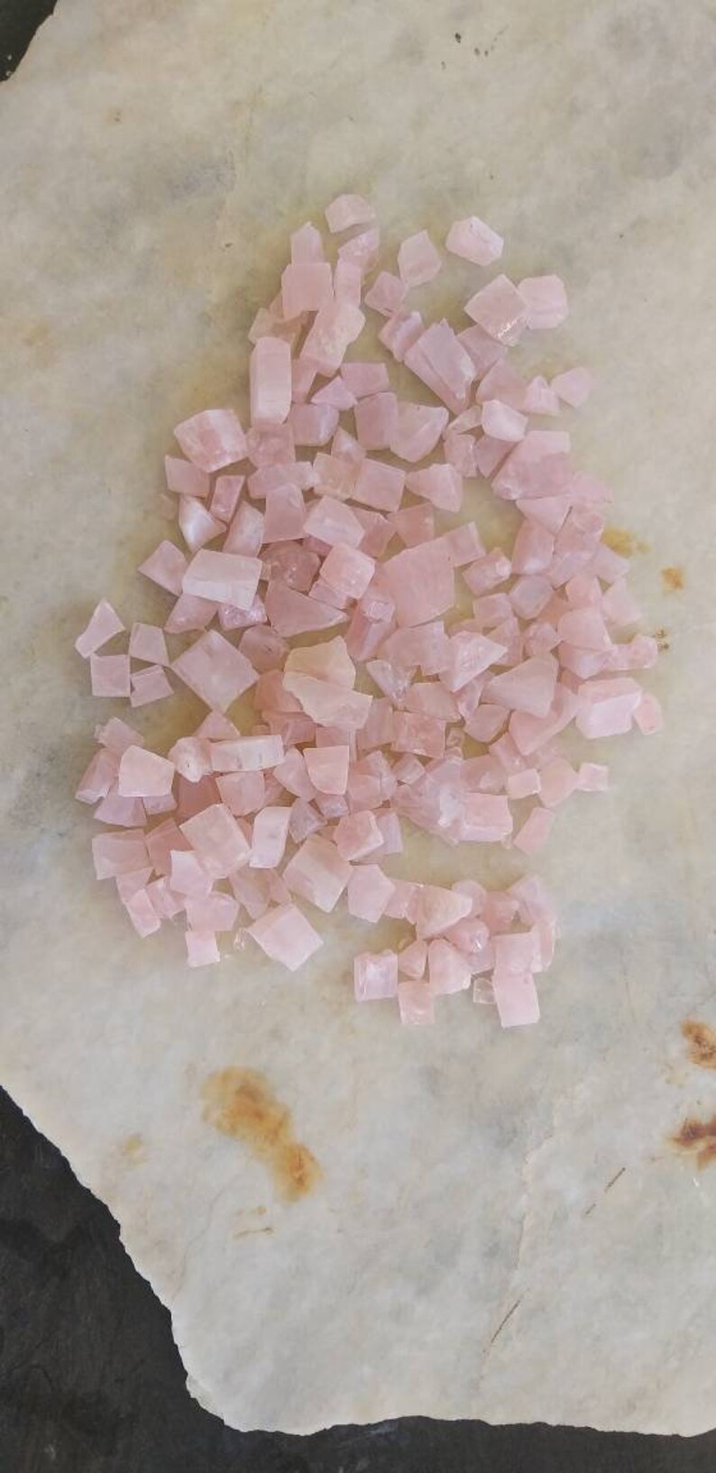 May include: A collection of small, pink rose quartz crystals. The crystals are irregularly shaped and have a translucent appearance.