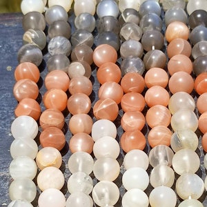 Puede incluir: Una hebra de cuentas de piedra de sol en varios tonos de blanco, melocotón y gris. Las cuentas son redondas y tienen un acabado liso y pulido.