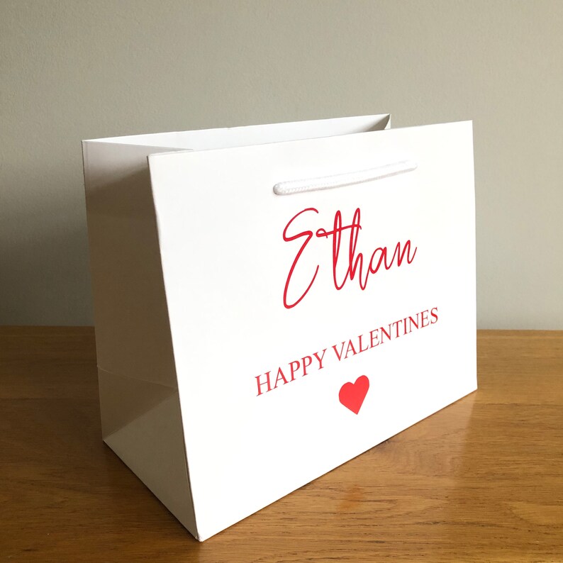 May include: White gift bag with red text that says "Ethan Happy Valentines" and a red heart.