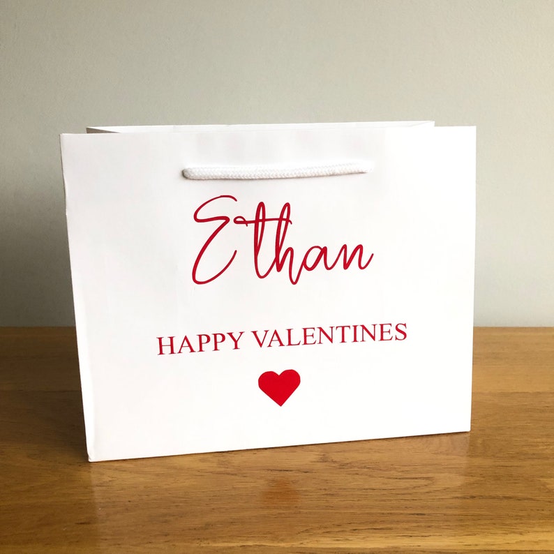 May include: White gift bag with red text that says "Ethan Happy Valentines" and a red heart.