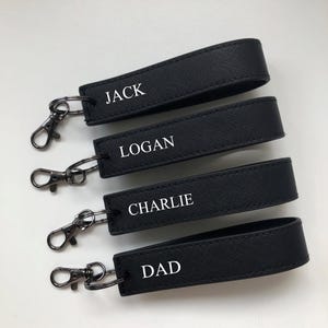 May include: Four black leather keychains with silver key rings. Each keychain has a different name printed in white: Jack, Logan, Charlie, and Dad.
