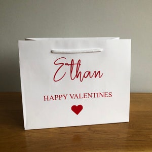 May include: White gift bag with a red heart and the text "Ethan Happy Valentines" printed on it.