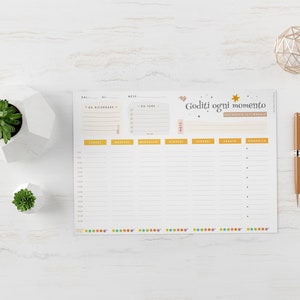 May include: A weekly planner with the text "Goditi ogni momento" in Italian. The planner has sections for each day of the week, with time slots and space for notes. A gold pen and geometric decoration are on the right.