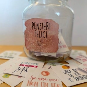 May include: A glass jar with a pink and white watercolor label that says "PENSIERI FELICI" filled with small white cards. The cards have inspirational messages written on them in Italian.
