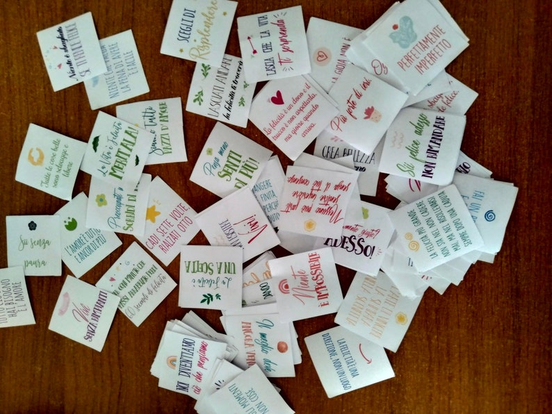 May include: A collection of small, colorful cards with inspirational quotes and phrases written in Italian. The cards are printed on white paper and have a variety of fonts and designs.