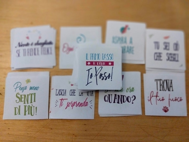 May include: A set of small white cards with inspirational quotes in Italian. The cards feature colorful illustrations and handwritten text. Some of the quotes include "Il primo passo e dire Io posso!" and "Penja meno Senti di piu!"