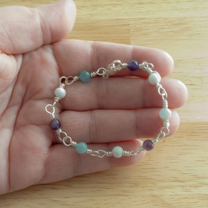May include: A silver chain bracelet with white, light blue, and purple beads.