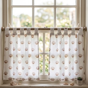 May include: A pair of white cafe curtains featuring a repeating pattern of small brown seashells. The curtains are made of a textured fabric and are hung from a wooden rod using fabric tabs. The design is light, airy, and semi-sheer.