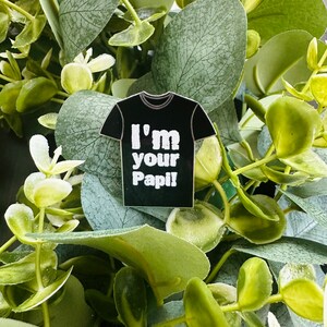 Puede incluir: Un pin de camiseta negra con el texto "I'm your Papi!" impreso en blanco.