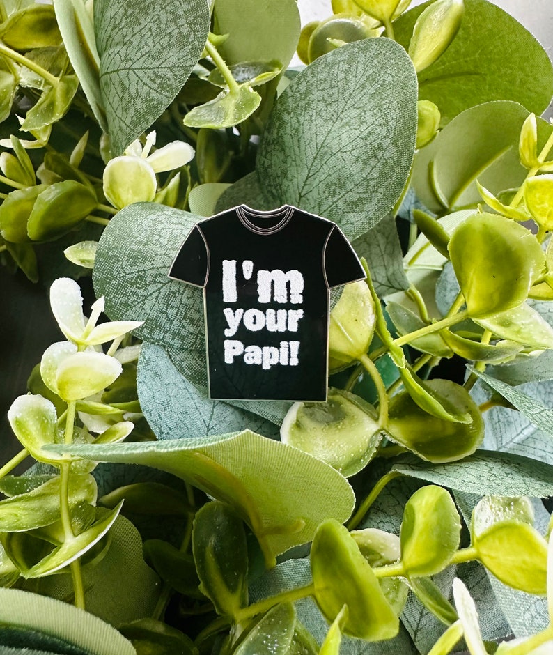 Puede incluir: Un pin de camiseta negra con el texto "I'm your Papi!" impreso en blanco.