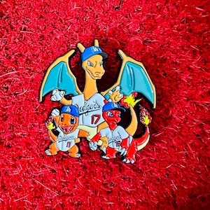 以下が含まれることがあります： 野球のユニフォームを着た3人の漫画のキャラクターが描かれた、カラフルなエナメルピン。オレンジ、赤、黄色のキャラクターは、青い帽子と「Dodgers」の文字と17番の数字が入った白いジャージを着ています。