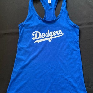 May include: A royal blue tank top with a racerback design. The word "Dodgers" is printed across the front in white script. The tank top is made of a soft material.