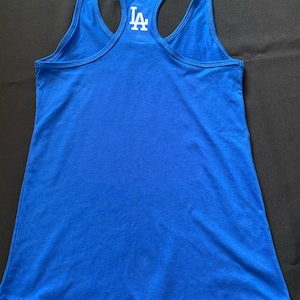 May include: Royal blue racerback tank top with the white letters "LA" on the back. The tank top is made of a soft material and has a scoop neck. The tank top is a sporty style.