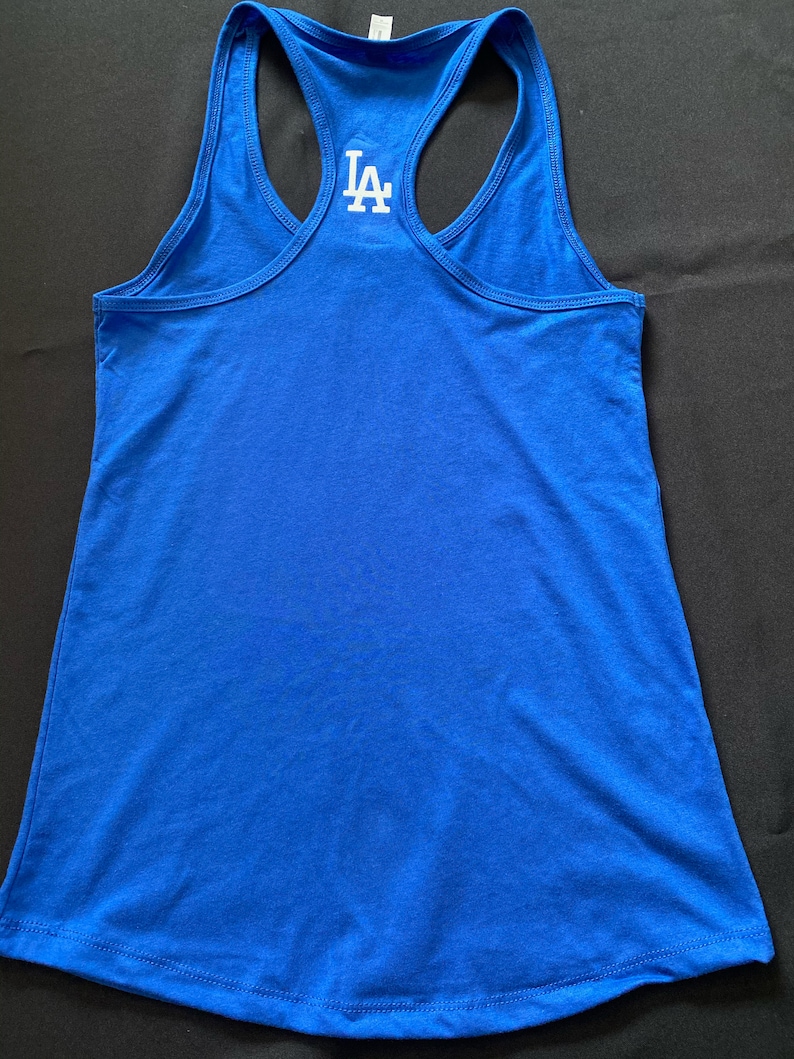 May include: Royal blue racerback tank top with the white letters "LA" on the back. The tank top is made of a soft material and has a scoop neck. The tank top is a sporty style.