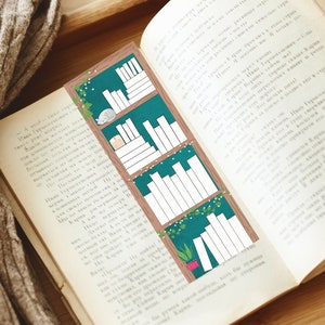May include: A green and brown bookmark with a bookshelf illustration featuring white books and green vines. The bookmark is placed in an open book.