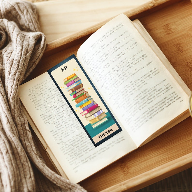 May include: A blue and green bookmark with a stack of colorful books and the text "THE TBR" and "XII" on it.