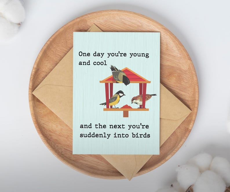 May include: A greeting card with the text "One day you're young and cool and the next you're suddenly into birds." The card features a birdhouse with three illustrated birds. The card is on a wooden tray with a brown envelope.