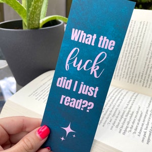 Puede incluir: Un marcap&aacute;ginas azul turquesa con texto rosa que dice "What the fuck did I just read??". El marcap&aacute;ginas tiene dos peque&ntilde;as estrellas blancas en la esquina inferior.