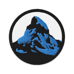 Pode incluir: Um remendo bordado azul e preto com uma silhueta de montanha em um círculo. A montanha é azul e o círculo é preto com um fundo branco.