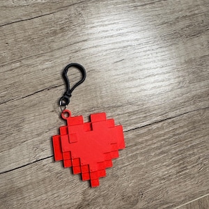 May include: A red pixelated heart keychain with a black clip.