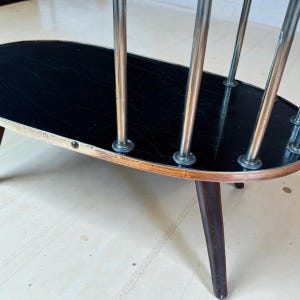 May include: Oval-shaped, mid-century modern side table with a black top and chrome supports. The table has a wooden frame with dark brown legs and a light-colored trim. A stylish piece for any living space.