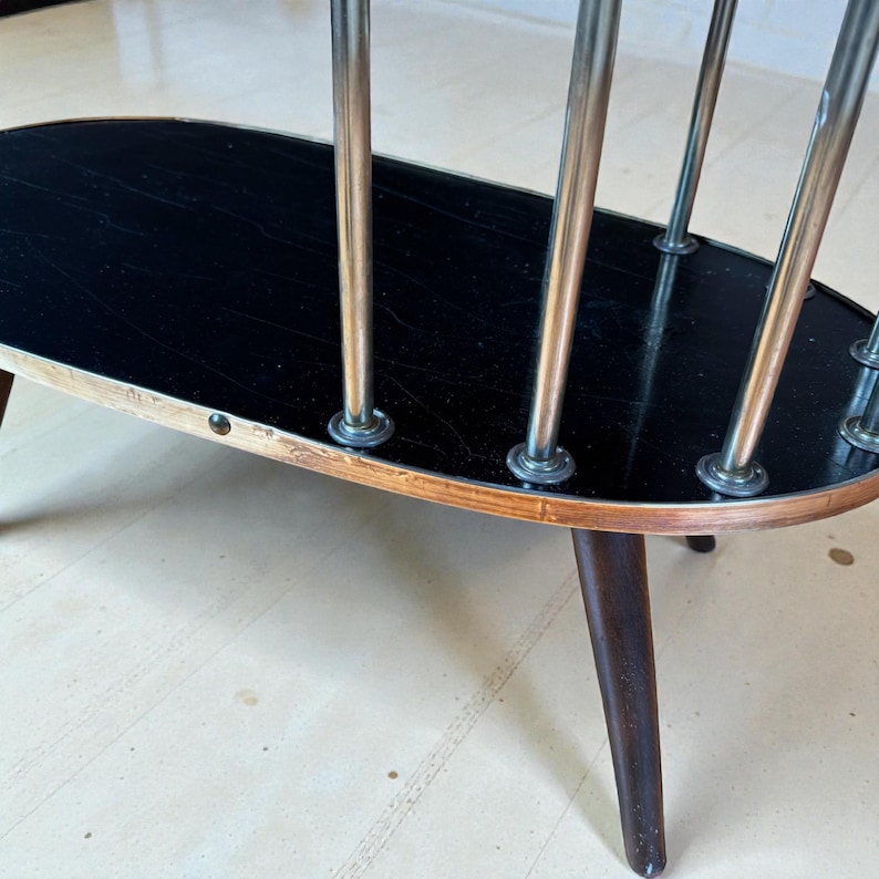 May include: Oval-shaped, mid-century modern side table with a black top and chrome supports. The table has a wooden frame with dark brown legs and a light-colored trim. A stylish piece for any living space.