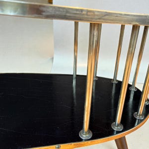 May include: A vintage oval-shaped side table with a black tabletop and a light wood frame. The table features vertical metal rods and a dark brown wooden leg. The design is mid-century modern.