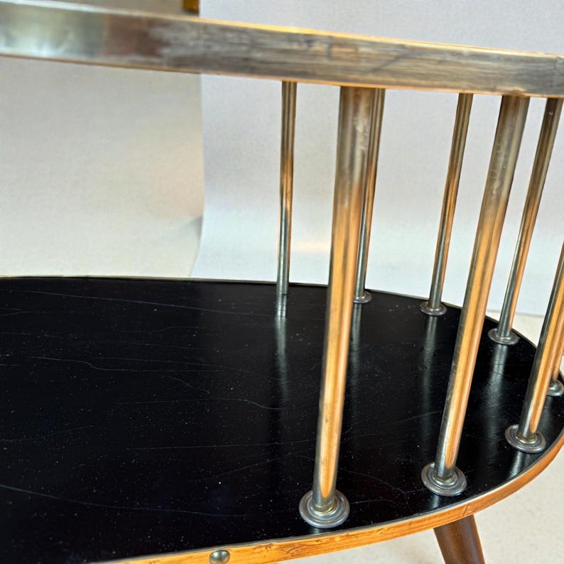May include: A vintage oval-shaped side table with a black tabletop and a light wood frame. The table features vertical metal rods and a dark brown wooden leg. The design is mid-century modern.