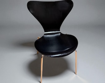 May include: A modern black chair with a distinctive, curved back and seat. The chair has a glossy finish and is supported by slender, gold-colored metal legs. The design is minimalist and elegant, suitable for various interior styles.